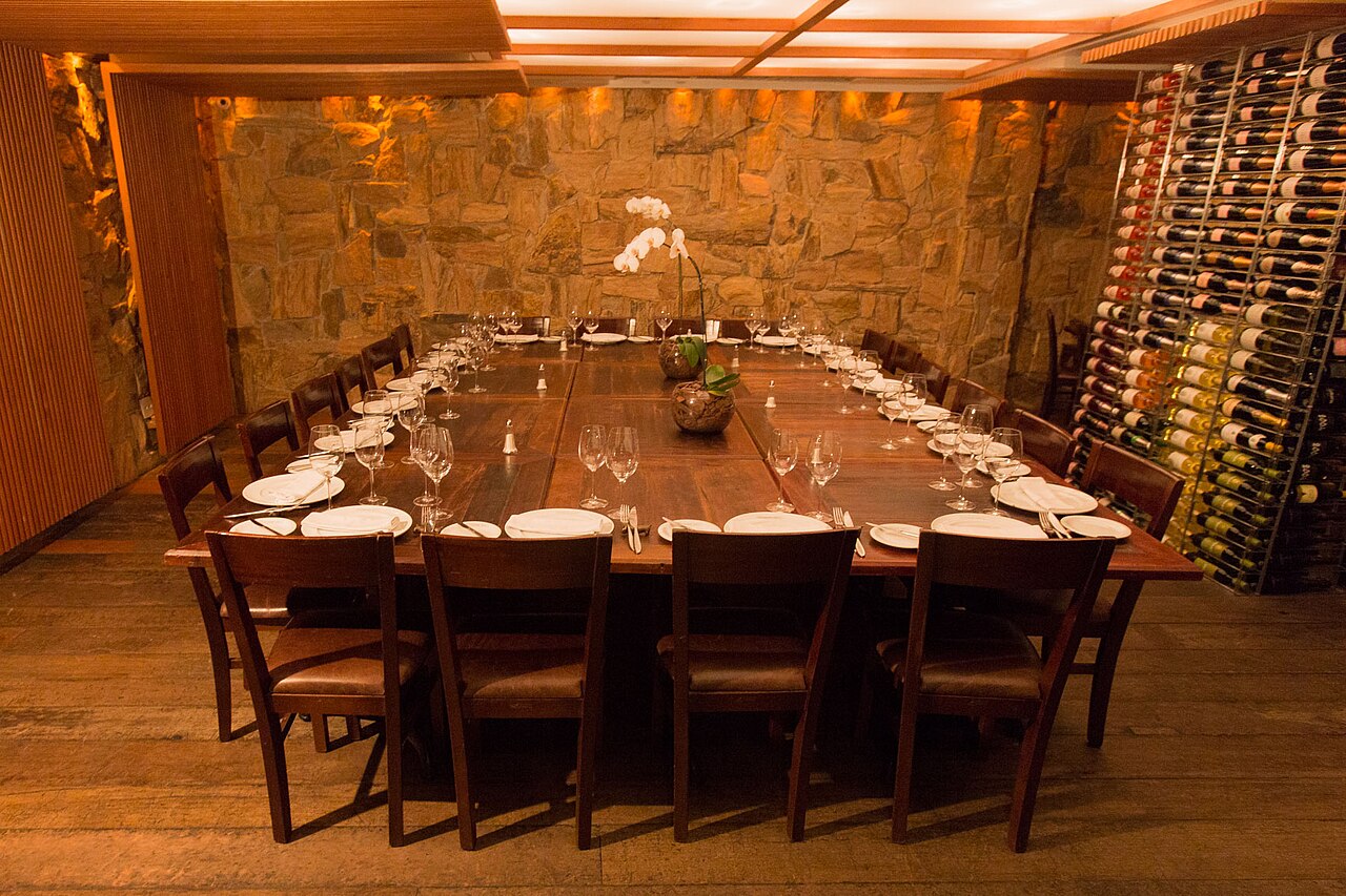 A private dining room set for a large party, with a long wooden table, wine glasses at every place and a wall of wine bottles.