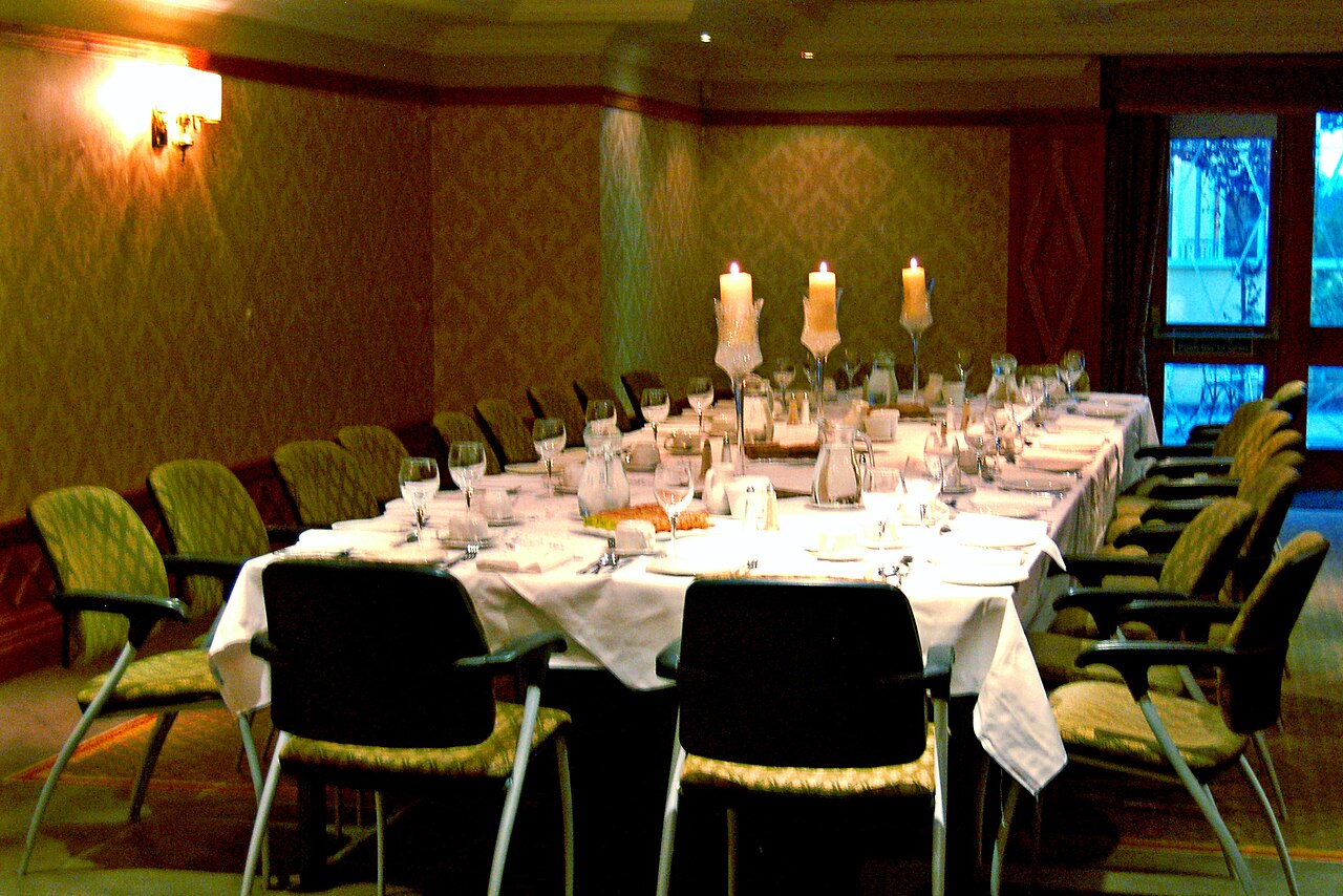 A private function room set for a wedding dinner: one long table with white cloths, candles and glasses at every place.