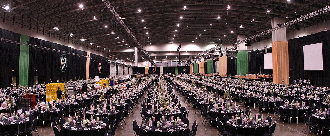 A vast hall set for one dinner: hundreds of round tables with flowers, and the crew still setting the last places.
